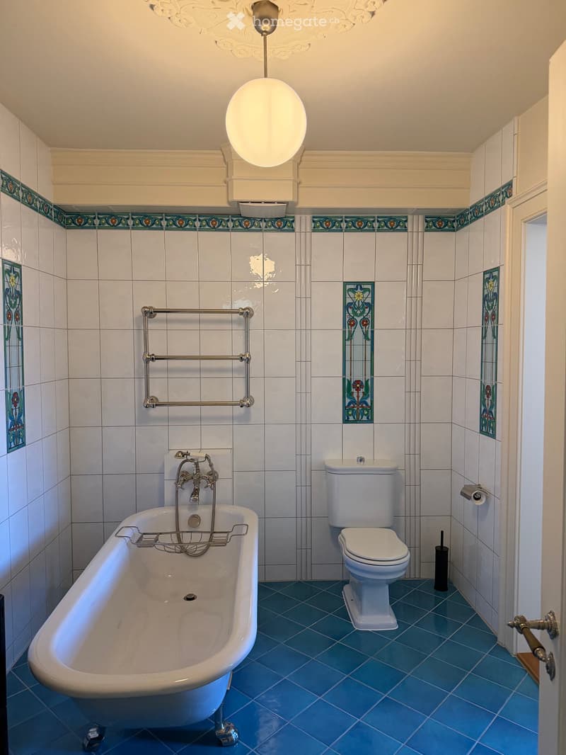Elegant bathroom with a clawfoot bathtub, toilet, decorative tiles, and a towel rack.