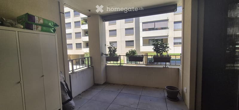 Balcony with tiled floor, metal railing, and potted plants. View of neighboring apartment building.