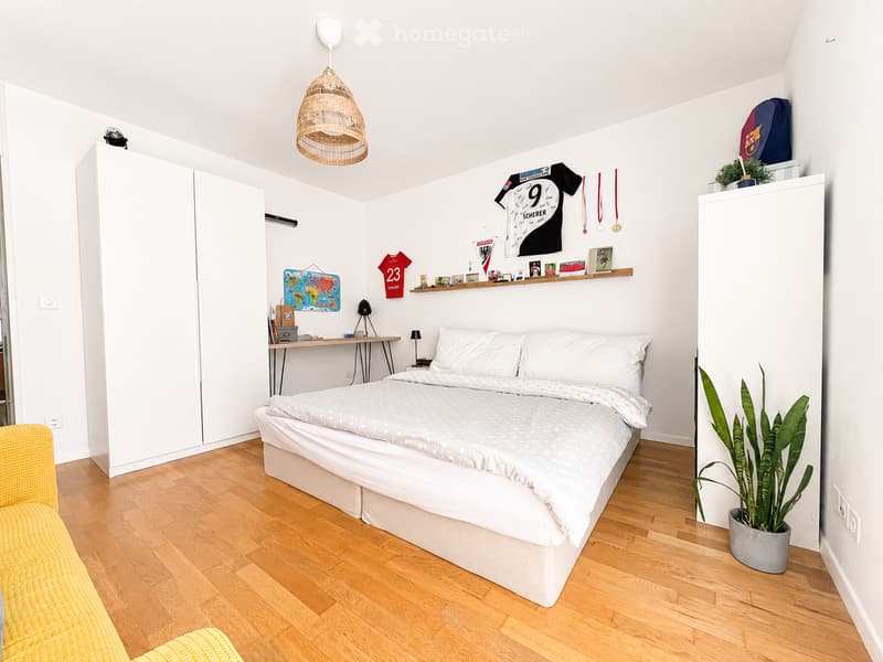 Modern bedroom with a white bed, wooden floor, wardrobe, desk, and decorative items on the wall.