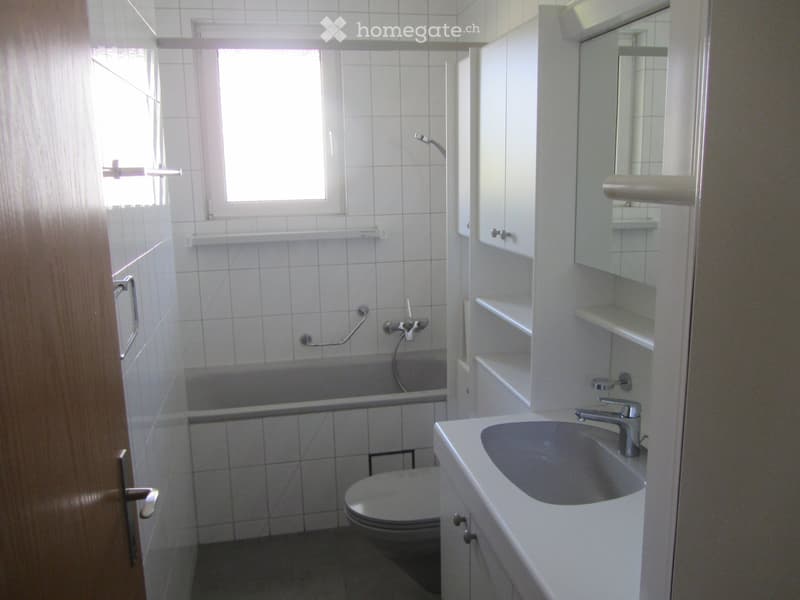 Modern bathroom with white tiles, a sink with a modern faucet, a mirror cabinet, a bathtub, and a toilet.