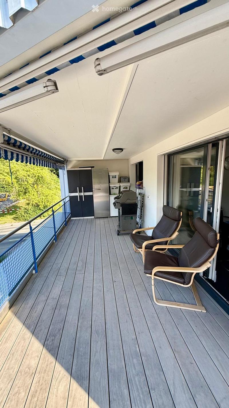 Balcony with wooden decking, two black leather chairs, a refrigerator, a grill, and a cabinet.