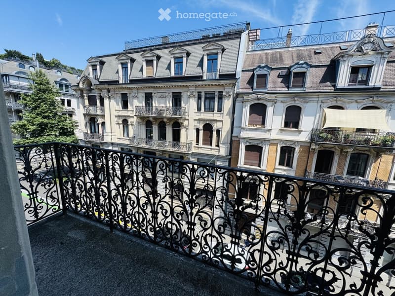 Balcony with ornate black metal railing overlooking a street lined with historic buildings featuring ornate facades, multiple windows, and decorative elements.
