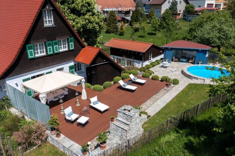 Aerial view of a residential property with a wooden deck, outdoor furniture, swimming pool, and surrounding greenery.