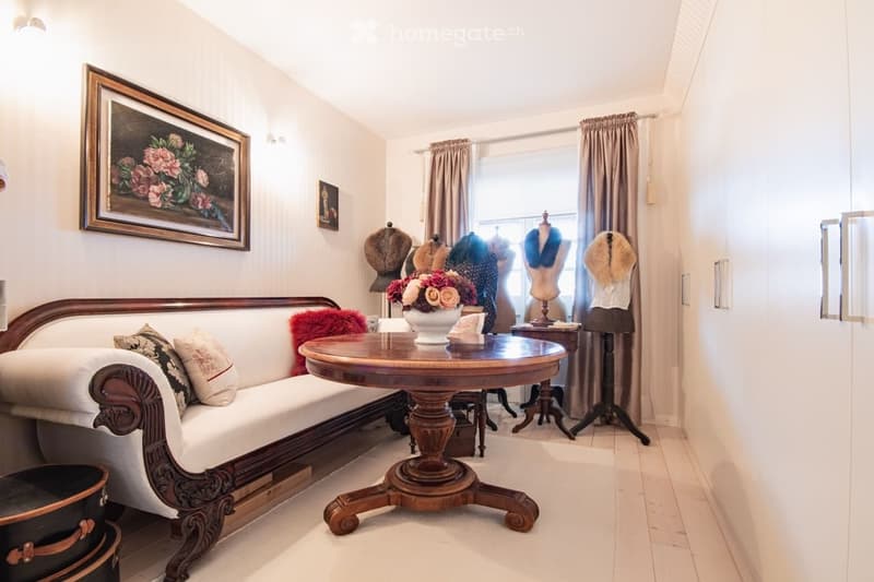 Elegant living room with a white sofa, wooden coffee table, floral vase, mannequins, and framed artwork.