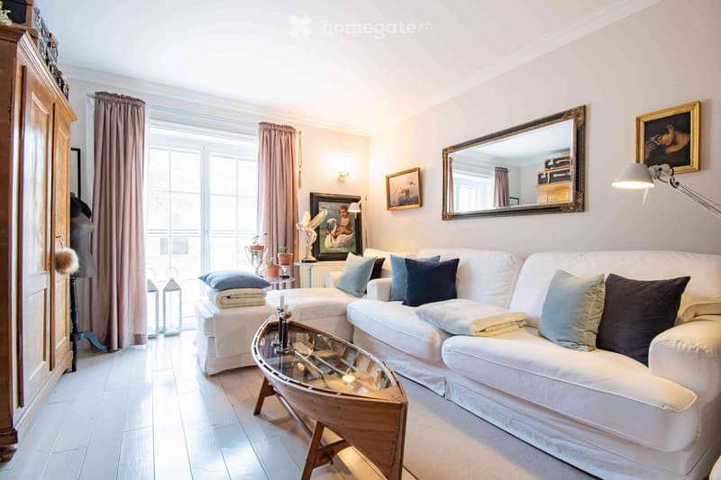 Bright living room with white sofa, glass coffee table, large mirror, picture frames, and decorative items.