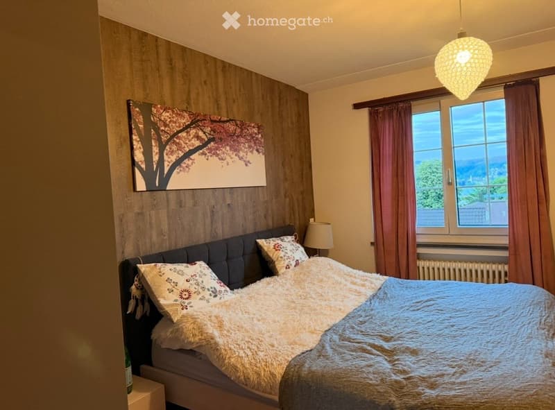 Cozy bedroom with a large bed, fluffy blanket, decorative pillows, nightstand with lamp, and a scenic view through the window.