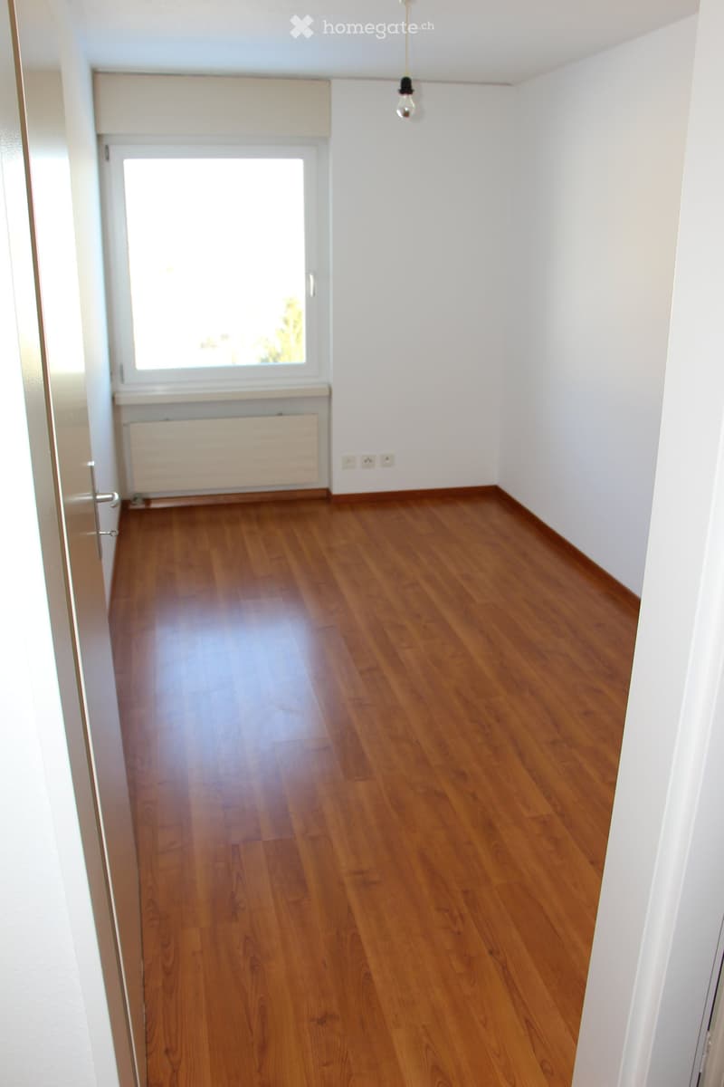 Empty room with wooden flooring, white walls, a window, and a radiator. No furniture or equipment is present.