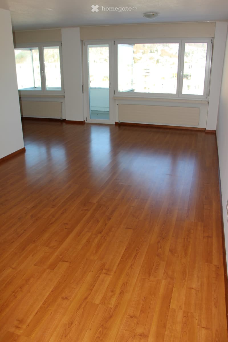Empty room with polished wooden flooring, white walls, large windows, and radiators.