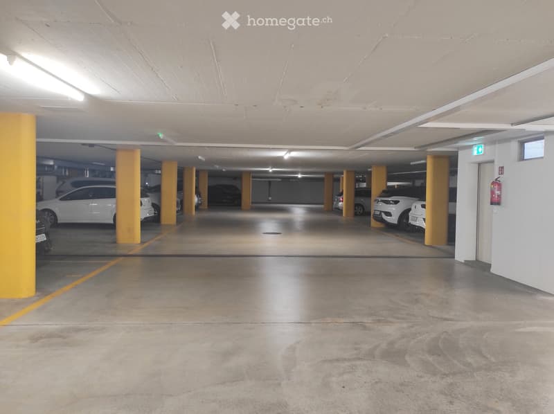Underground parking area with several parked cars, yellow support pillars, and a clean concrete floor.
