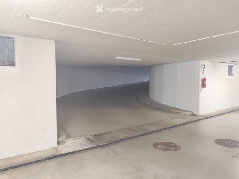 {"type": "Garage", "objects": [], "description": "Empty underground garage with concrete floors, white walls, and fluorescent lighting. Features a fire extinguisher mounted on the wall and a few drainage grates on the floor.", "localized_descriptions": {"