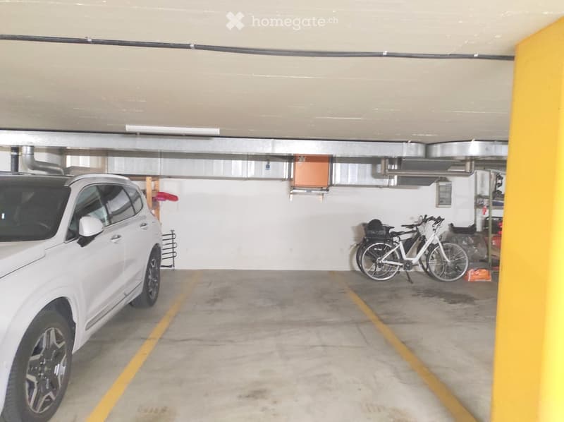 Underground parking area with a white SUV and a bicycle parked inside.