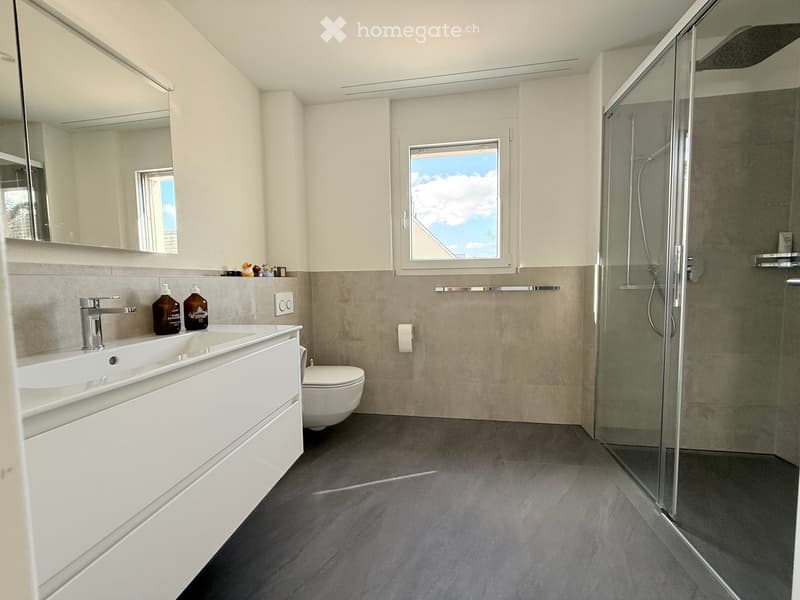 modern bathroom with white tiles, glass shower, white vanity, toilet, mirror, and a window