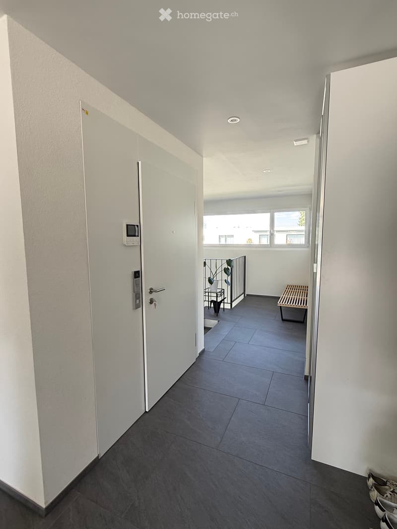 Empty hallway with white walls, gray floor, white doors, and a balcony with a railing