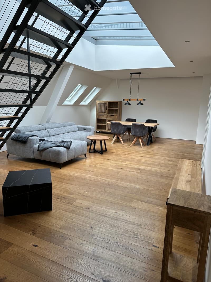 Modern living and dining area with wooden flooring, grey sectional sofa, coffee table, dining table with chairs, and a wooden cabinet.