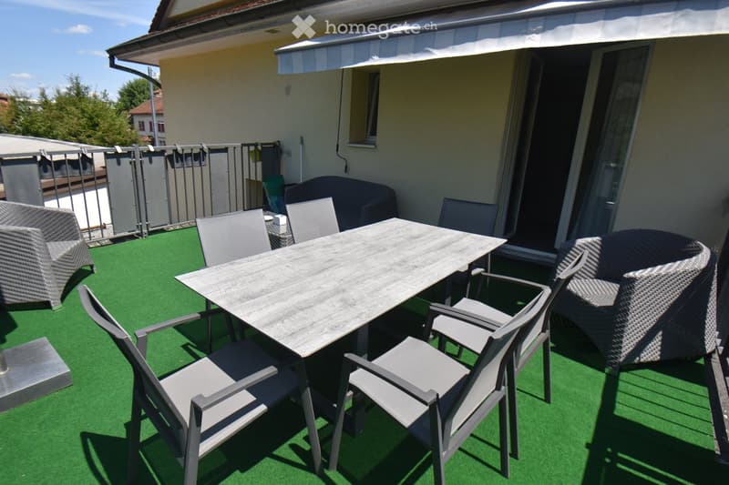 Balcony with green artificial turf, wooden table, several chairs, and a wicker sofa.