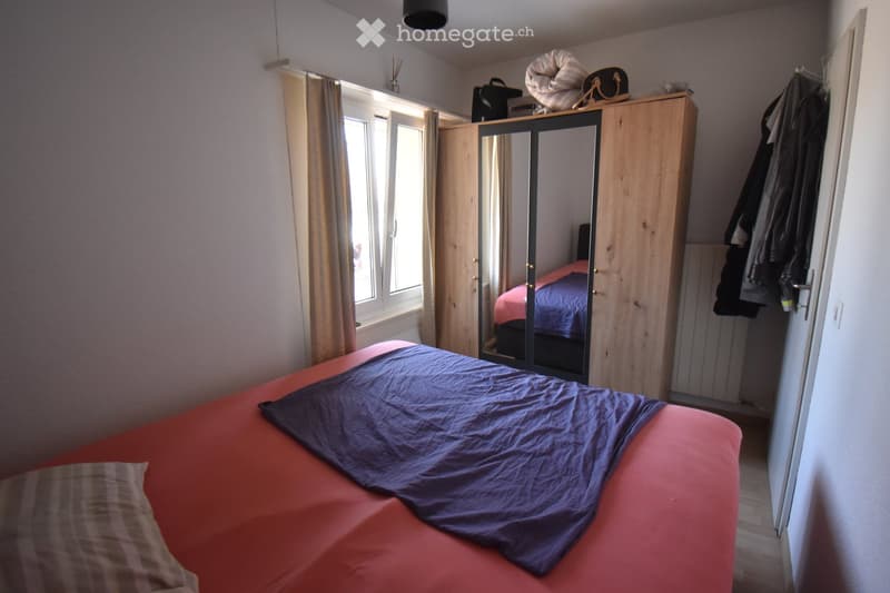 Bedroom with a red bed, blue blanket, mirror wardrobe, and window with curtains.