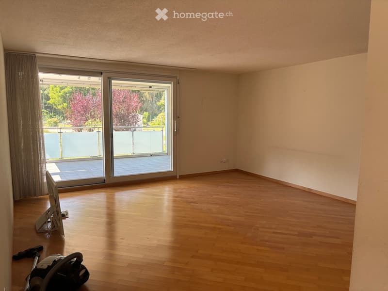 Empty room with wooden flooring, large sliding glass doors leading to a balcony, and a view of greenery outside.