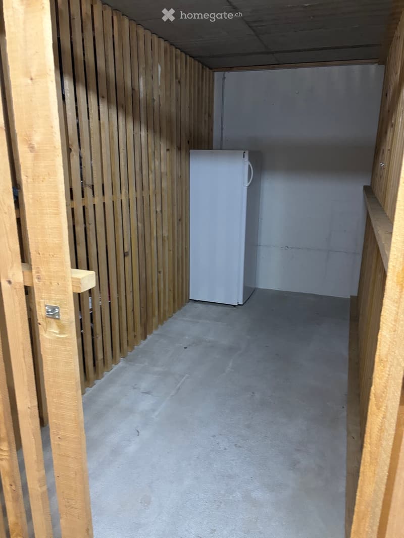 A partially constructed room with exposed wooden framing, a single refrigerator, and unfinished concrete flooring.