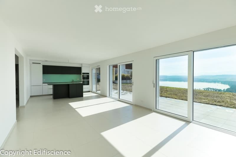 Modern, open-plan kitchen and living space with large windows offering a scenic view, white cabinets, central island, and tiled flooring.