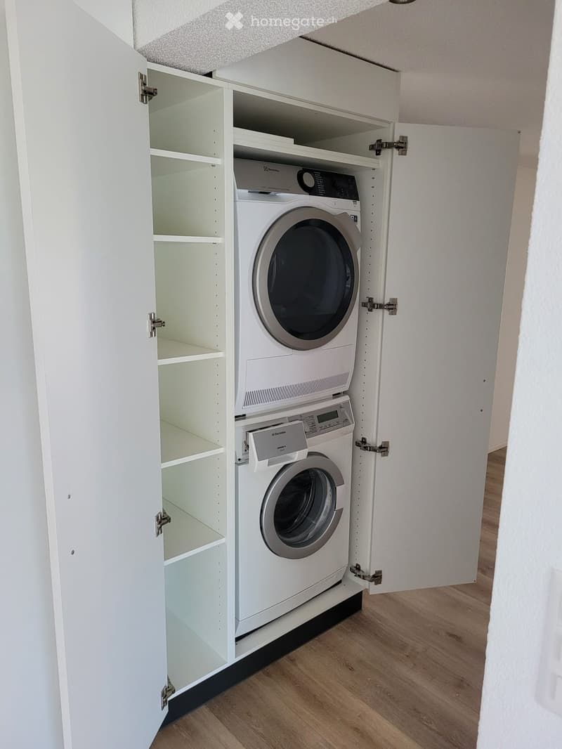 A compact laundry area with a washing machine and dryer installed in a built-in cabinet with open shelving.
