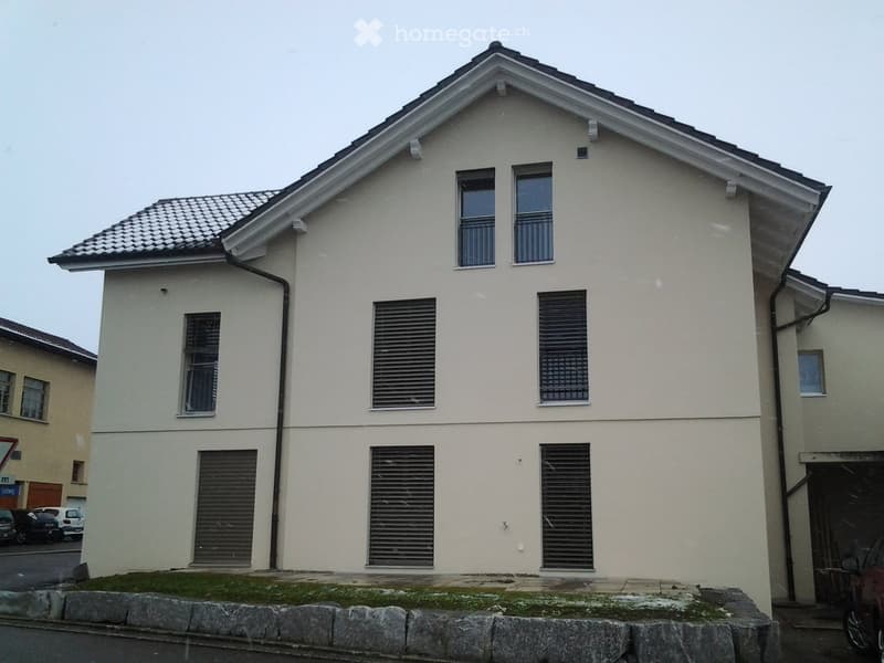 Two-story house with beige exterior, multiple windows, and a tiled roof.