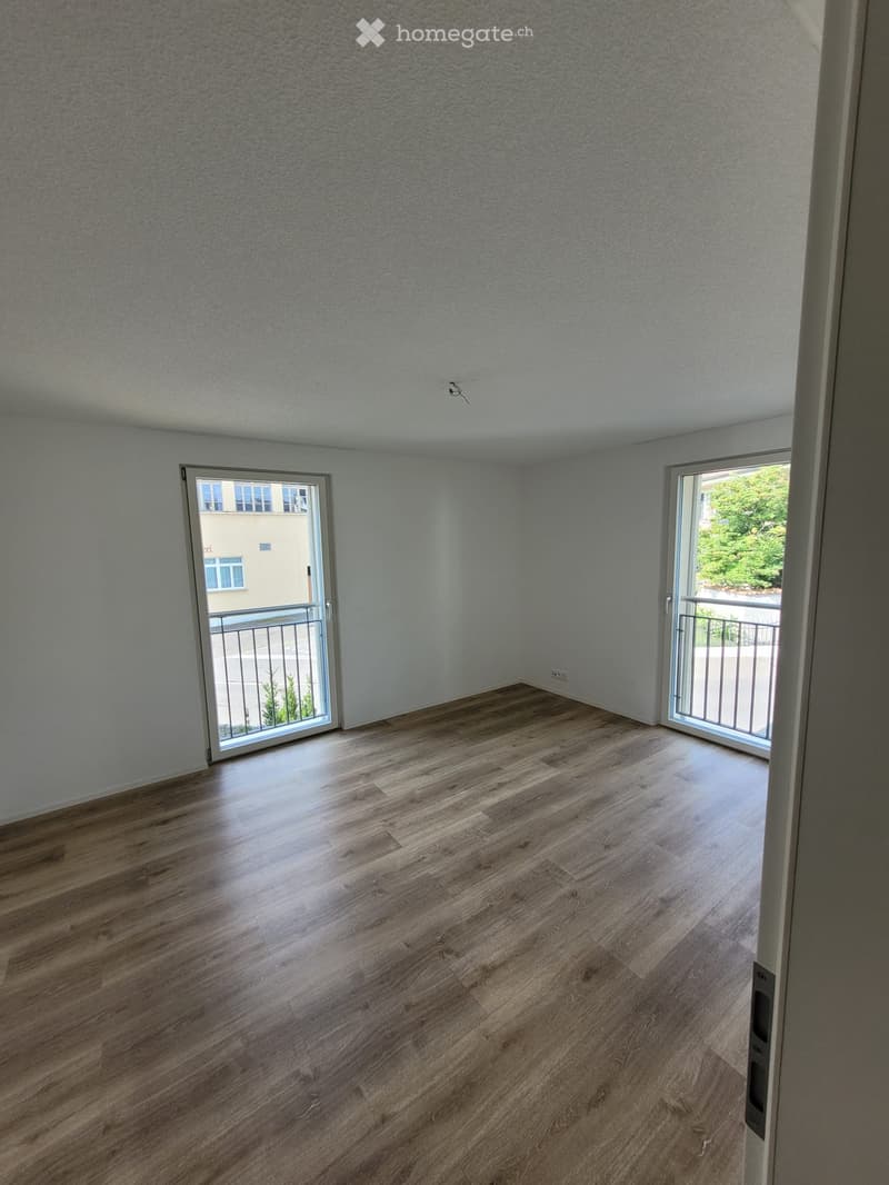 Empty room with wooden flooring, white walls, and two sliding glass doors leading to a balcony.