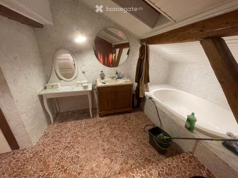 Bathroom with a bathtub, sink, vanity, and mirrors. The room features a tiled floor and wooden ceiling beams.