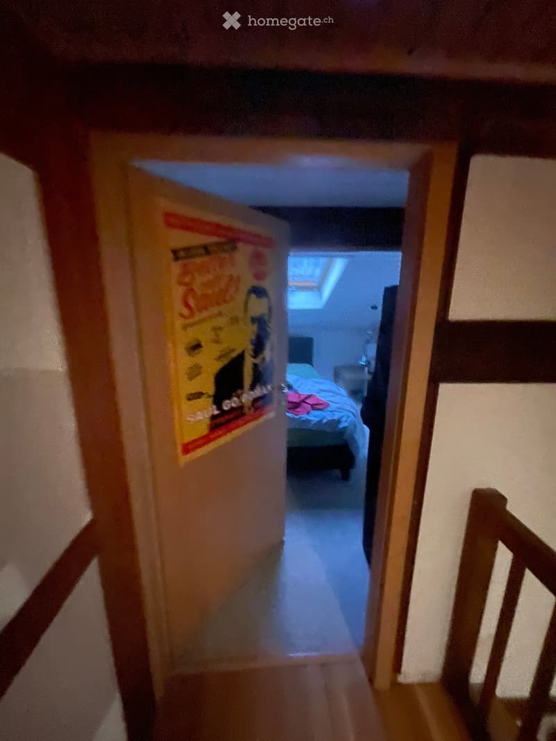 A narrow hallway with wooden walls and a partially open door leading to a bedroom with a bed and a poster on the wall.