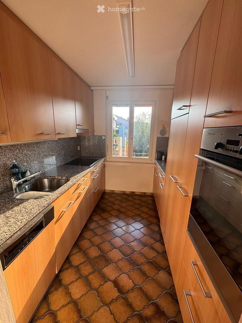 Modern kitchen with wooden cabinets, granite countertop, stainless steel sink, and built-in oven. Features a window with a view of the outside.