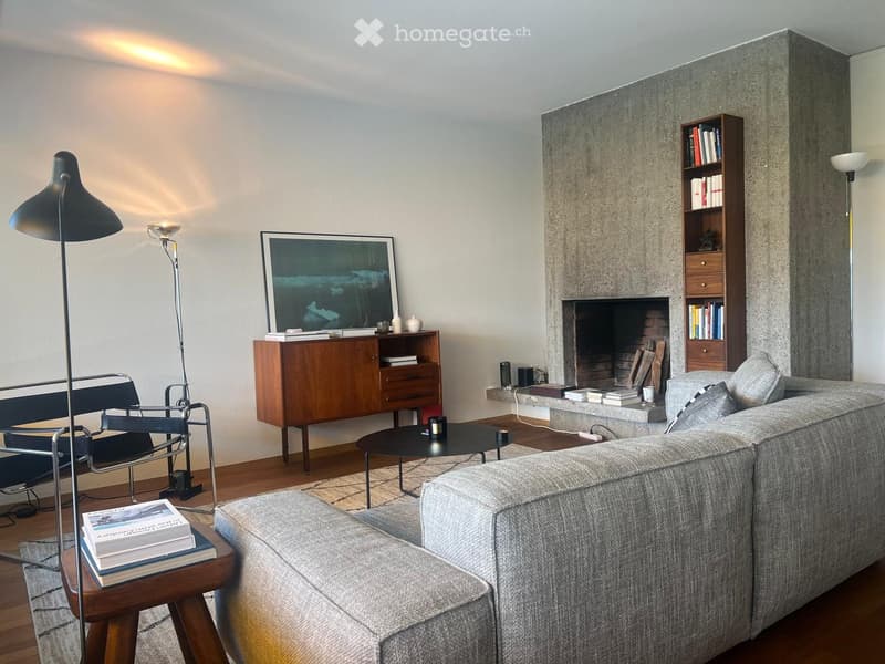 Modern living room with a grey sectional sofa, coffee table, fireplace, bookshelf, and floor lamp.