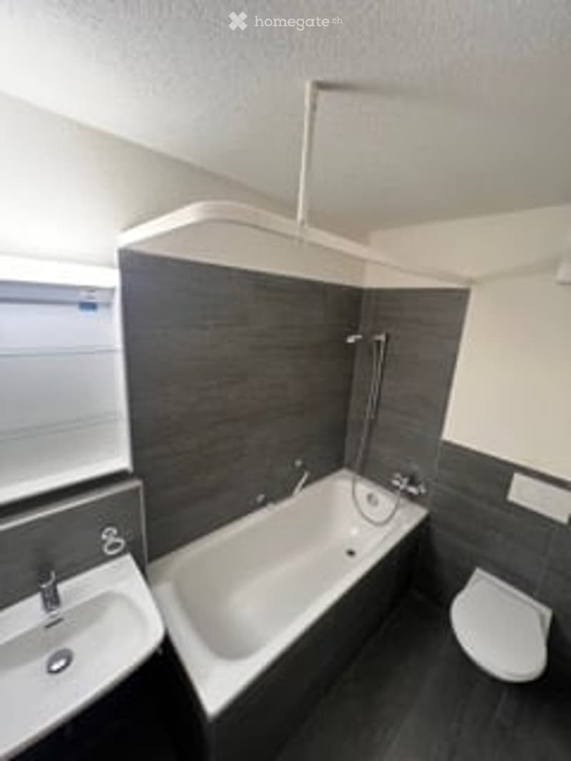 Modern bathroom with a bathtub, toilet, sink, and sleek dark grey tiles.