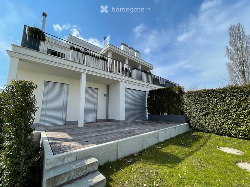 Modern two-story house with white exterior, large garage, raised wooden deck, and balcony on the upper level.