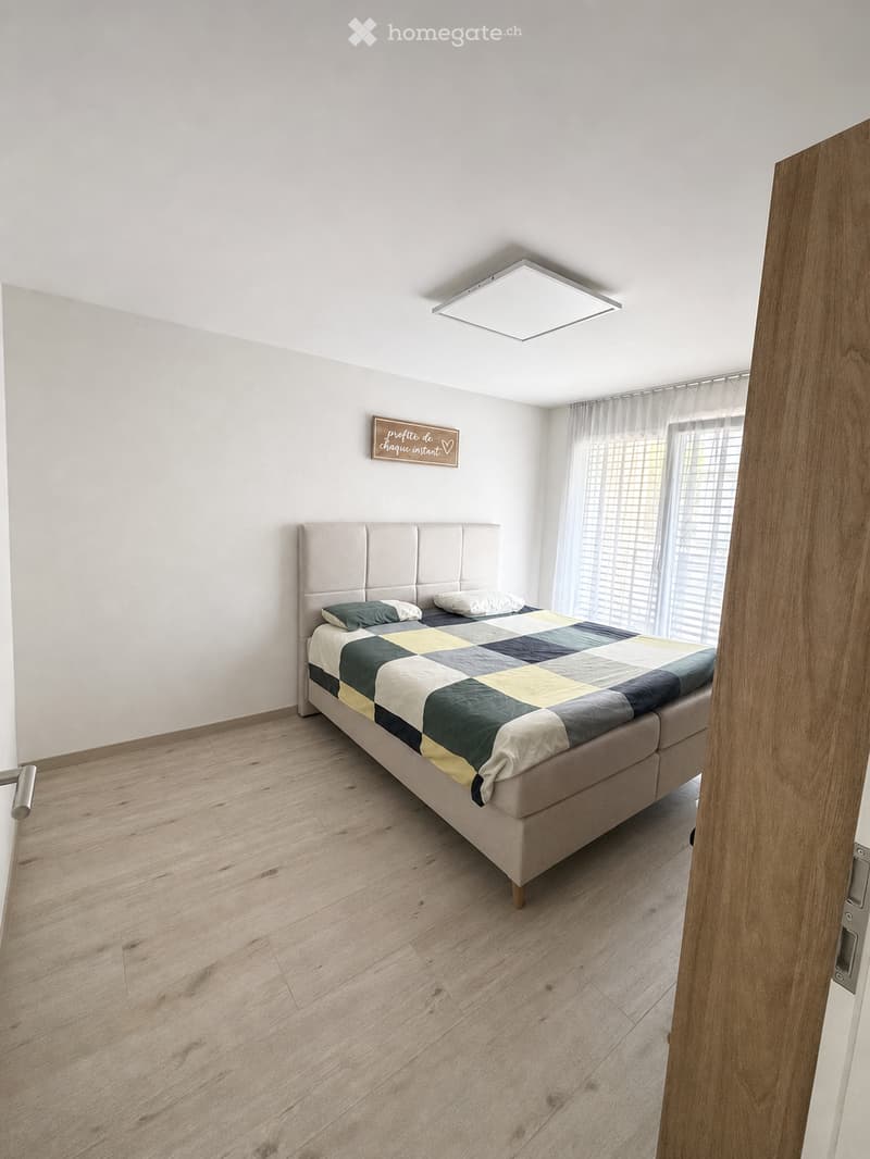 Modern bedroom with a large bed, beige headboard, checkered duvet, and wooden flooring.