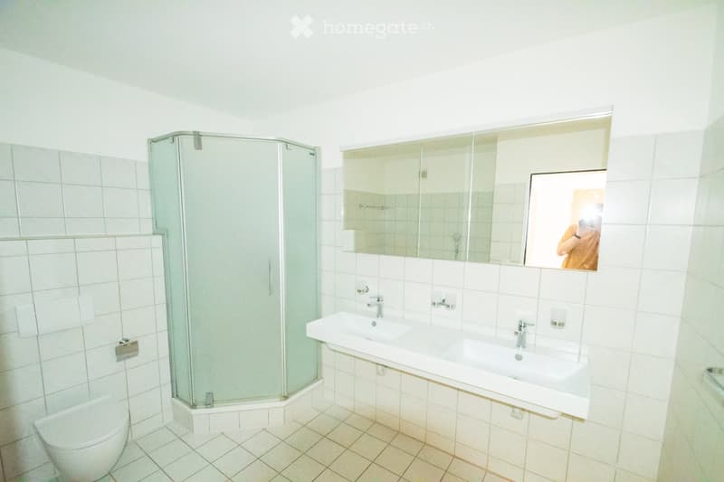 Modern bathroom with white tiles, a glass-enclosed shower, a double sink, and a large mirror above the sink.