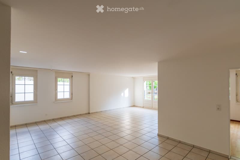 Empty room with tiled floor and white walls, featuring multiple windows and a door leading outside.
