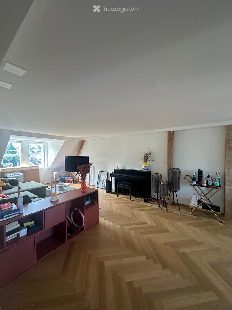 A modern, well-lit living room with wooden flooring, a red cabinet, a sofa, a piano, and decorative items.