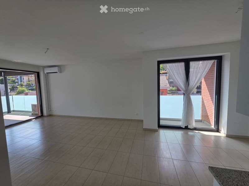 Empty room with tiled floor, white walls, large sliding glass doors leading to a balcony, and an air conditioning unit mounted on the wall.