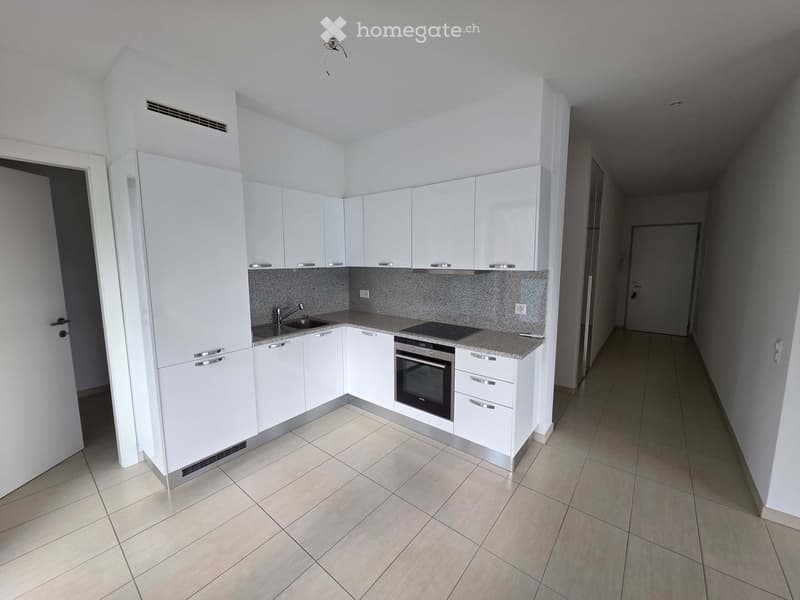 Modern kitchen with white cabinets, a sink, a faucet, an oven, and a countertop, featuring tiled flooring and a hallway leading to another room.