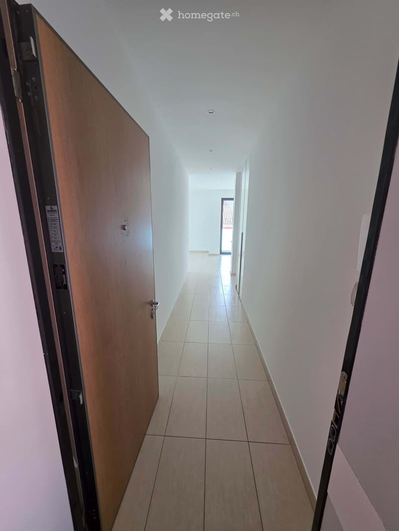 Empty hallway with tiled floor, white walls, and recessed ceiling lighting. Doors visible on both sides.
