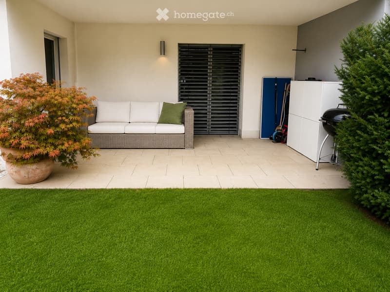 Modern outdoor patio with a white sofa, green cushions, a barbecue, potted plants, and a neatly trimmed lawn.