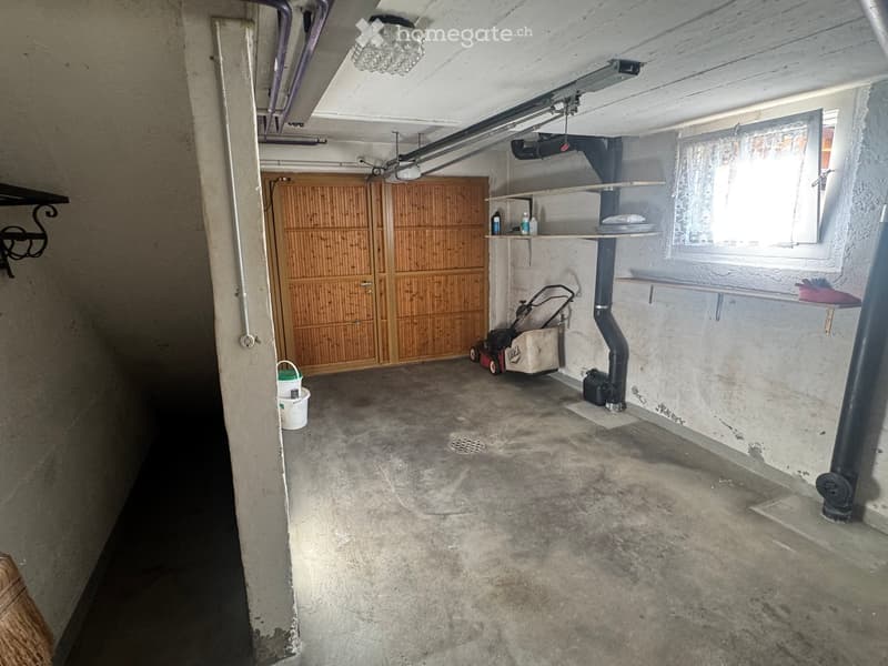 Empty basement with concrete floor, wooden cabinet, shelves, and a window letting in natural light.