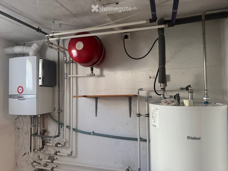Utility room with a water heater, boiler, and various pipes and connections.