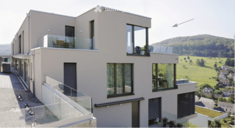 Modern, multi-story building with large windows and glass balconies overlooking a scenic countryside view.