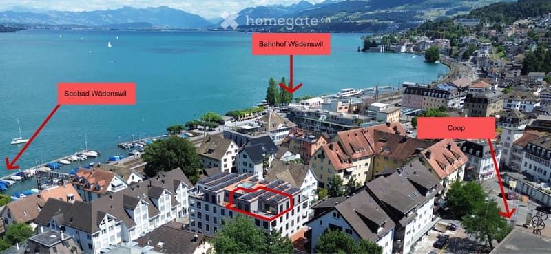 Aerial view of a town with a lake, mountains, and labeled landmarks including a train station, a swimming area, and a supermarket.