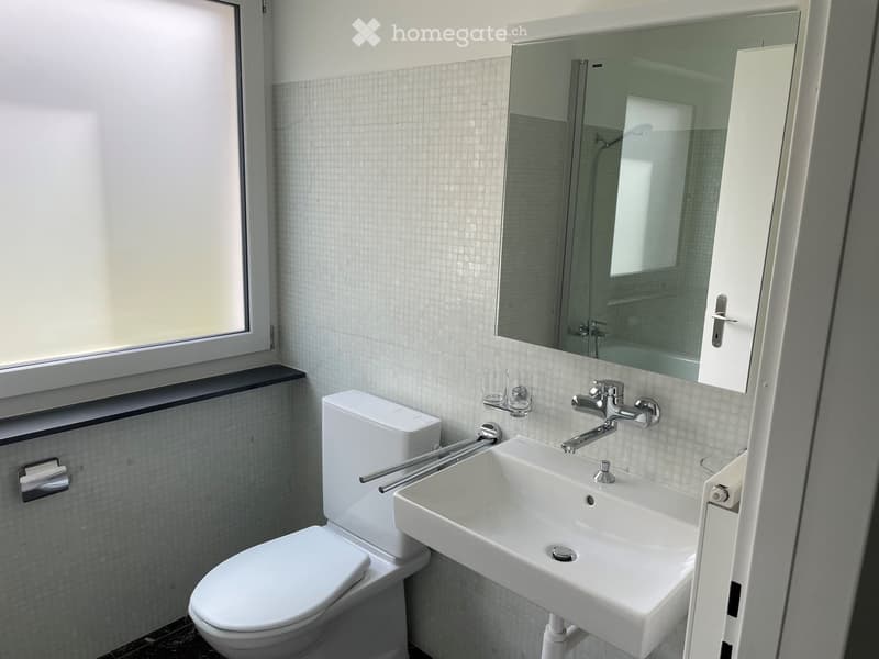 Modern bathroom with white tiles, a toilet, a sink with a chrome faucet, a large mirror, and two cups on a shelf.