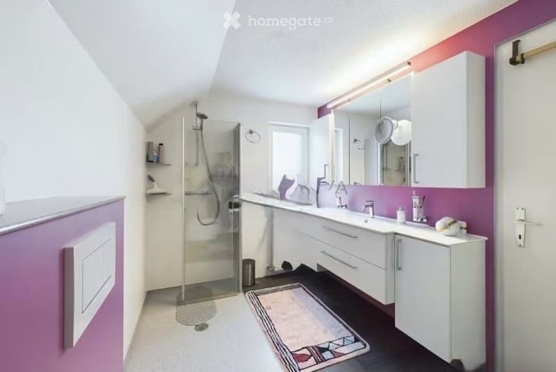 Modern bathroom with white cabinets, a double sink, a large mirror, a glass-enclosed shower, and a decorative rug on the dark floor.