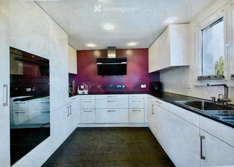 Modern kitchen with white cabinets, stainless steel sink, and built-in oven. Features a dark countertop and sleek design.