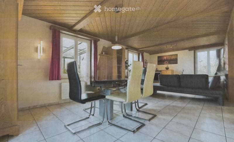 A cozy living and dining area with a wooden ceiling, tiled floor, and large windows. Features a black sofa, a glass dining table with modern chairs, and a wooden cabinet.