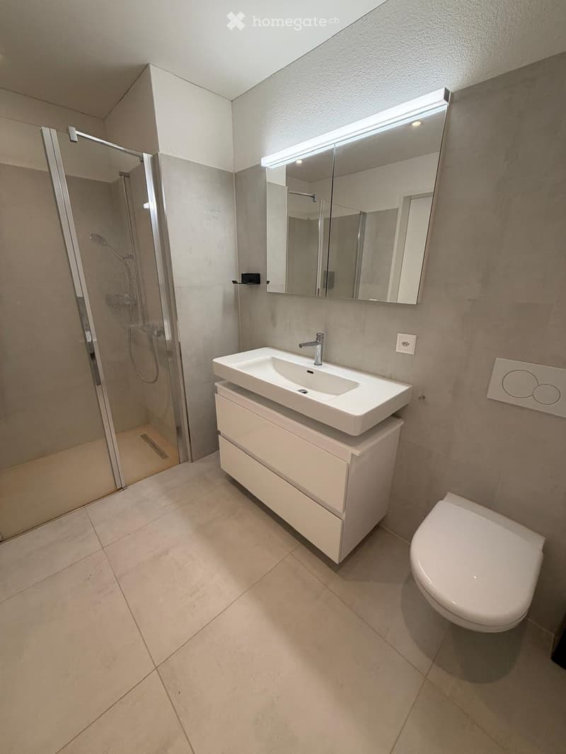 Modern bathroom with a white sink, toilet, large mirror with LED lighting, and a glass-enclosed shower area.