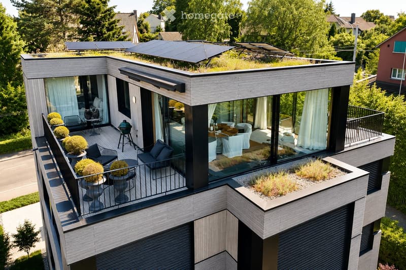 Modern rooftop terrace with wooden decking, lounge chairs, small table, potted plants, and a dining area inside with white chairs and a table.